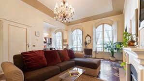 A living room with a brown sectional sofa, a glass coffee table, a chandelier, and a fireplace. - Perfect Heart of Florence-Super Upscale Location-Roomy-Washer-Elevator (Florence)