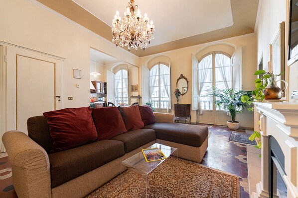 A living room with a brown sectional sofa, a glass coffee table, a chandelier, and a fireplace. - Perfect Heart of Florence-Super Upscale Location-Roomy-Washer-Elevator (Florence)