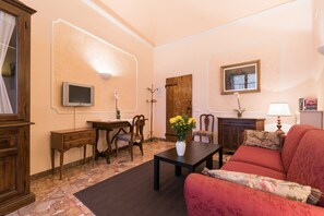 A living room with a sofa, a coffee table, a TV, a wooden cabinet, and a door. - Best Upscale Historic Center-Terrace-AC-Washer-Lift (Florence)