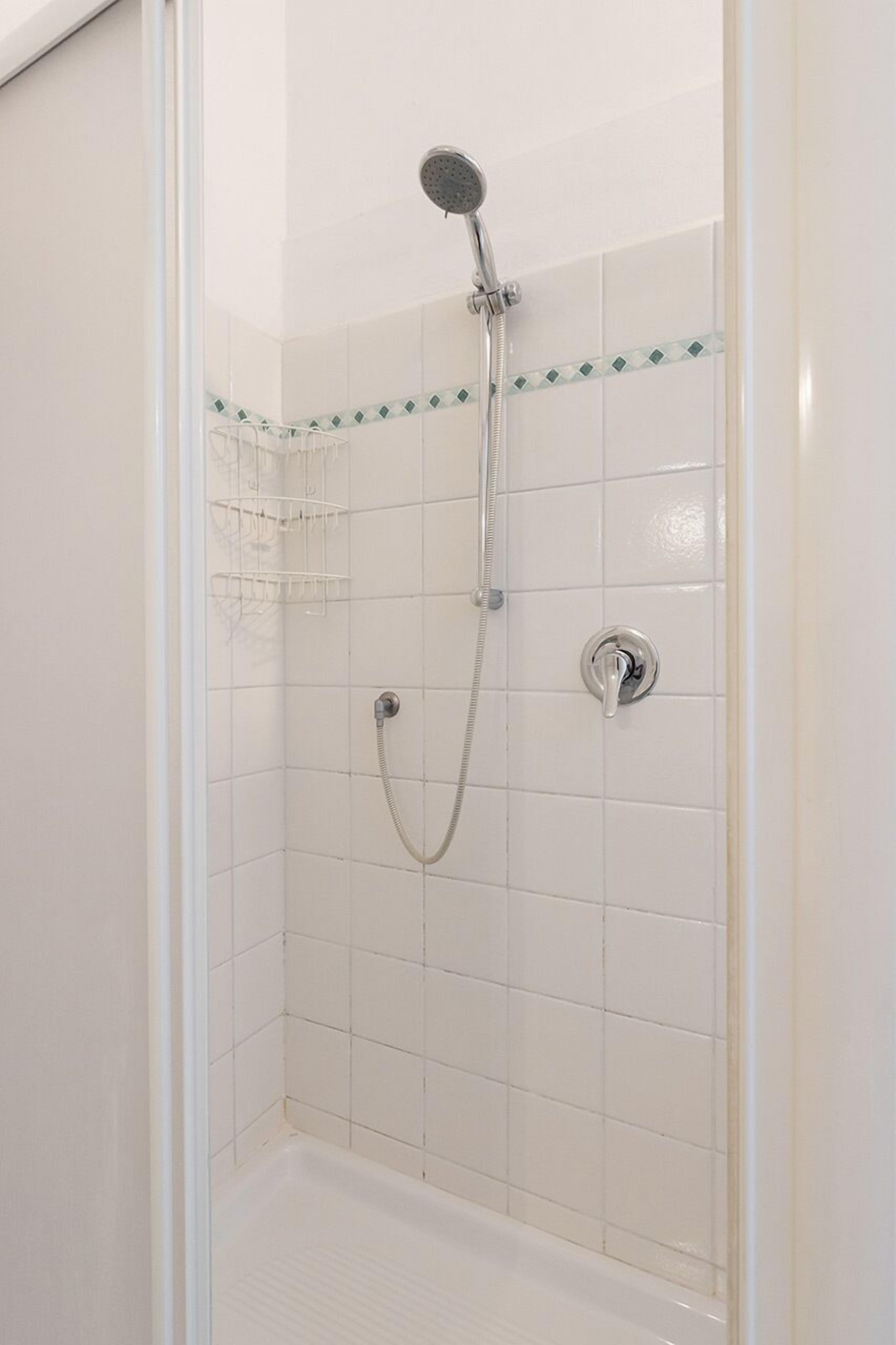 Une douche équipée d’un pommeau de douche à main et d’un robinet fixé au mur.