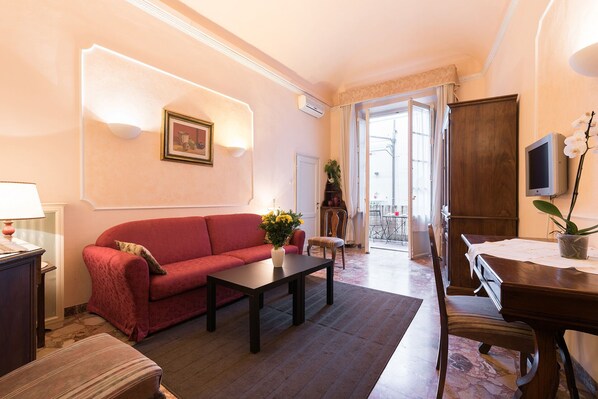 A living room with a red sofa, a coffee table, a TV, and a dining area with a table and chairs. - Best Upscale Historic Center-Terrace-AC-Washer-Lift (Florence)