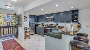 A modern kitchen with dark blue cabinets, stainless steel appliances, a granite countertop, and a red rug leading to a balcony. - 🏔️Ski-In, Ski-Out Condo~Hot Tub~Interlude 203🏔️ (Snowmass Village)