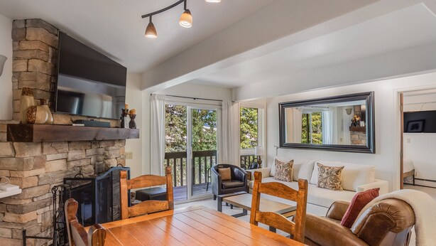 A spacious living room with a stone fireplace, wooden dining table, leather sofas, and a large flat-screen TV mounted on the wall. - 🏔️Ski-In, Ski-Out Condo~Hot Tub~Interlude 203🏔️ (Snowmass Village)