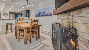 A modern kitchen with dark cabinets, a wooden dining table, and a stone fireplace. - 🏔️Ski-In, Ski-Out Condo~Hot Tub~Interlude 203🏔️ (Snowmass Village)