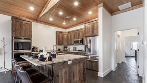 Une cuisine dotée de meubles en bois, d’appareils électroménagers en acier inoxydable et d’un coin bar avec des tabourets.