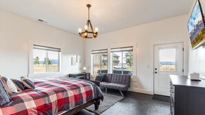 Une chambre à coucher comprenant un lit, un banc, une commode et de grandes fenêtres donnant sur l’extérieur.