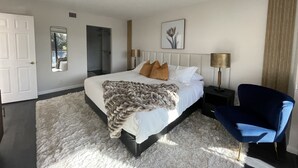A bedroom with a bed, a chair, a bedside table, a lamp, a mirror, and a door. - Lux King Bed Suite, Modern Condo Delray Beach. DRClub - 40% Off Fall & Holidays (Delray Beach)