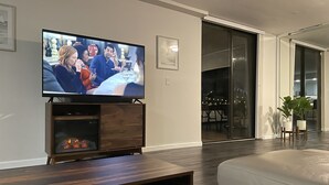 A modern living room with a flat-screen TV on a wooden stand, a fireplace, and a sliding glass door leading to a dining area. - Lux King Bed Suite, Modern Condo Delray Beach. DRClub - 40% Off Fall & Holidays (Delray Beach)