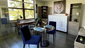 A modern living room with a glass dining table, two blue chairs, a white cabinet, and a large window with a view of palm trees. - Lux King Bed Suite, Modern Condo Delray Beach. DRClub - 40% Off Fall & Holidays (Delray Beach)