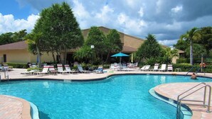 A swimming pool with lounge chairs and umbrellas, surrounded by palm trees and a building in the background. - Lux King Bed Suite, Modern Condo Delray Beach. DRClub - 40% Off Fall & Holidays (Delray Beach)