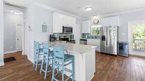 Una cocina moderna con armarios blancos, electrodomésticos de acero inoxidable y una isla central con taburetes de bar.