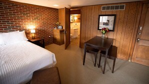 A hotel room with a brick wall, a wooden desk, a bed, and a bathroom visible through an open door.