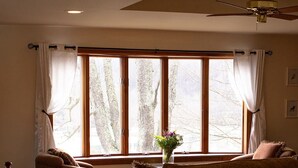 A spacious living room with a large window, a ceiling fan, and a wooden staircase.