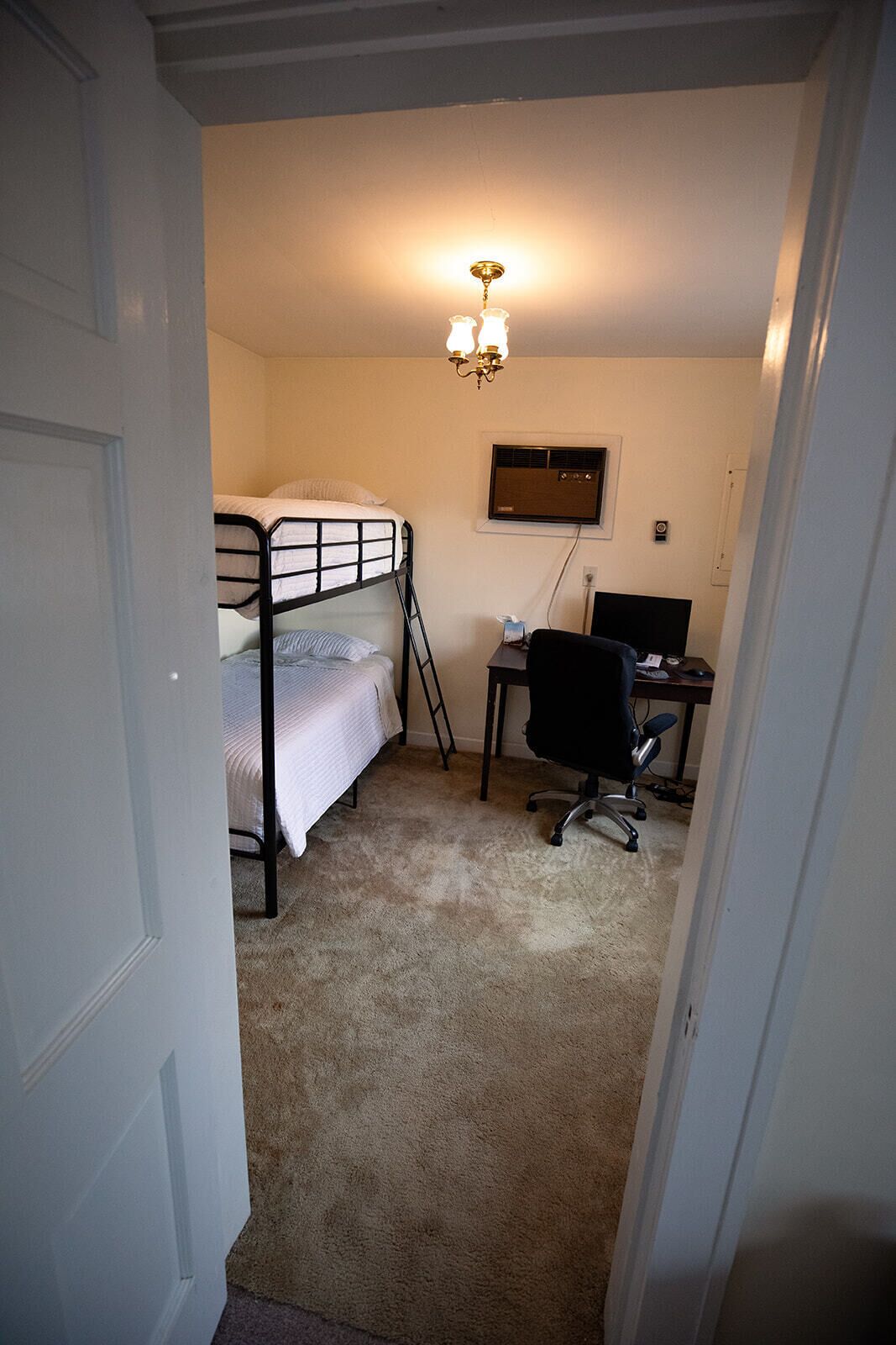A bedroom with bunk beds, a desk, a chair, and a ceiling light.