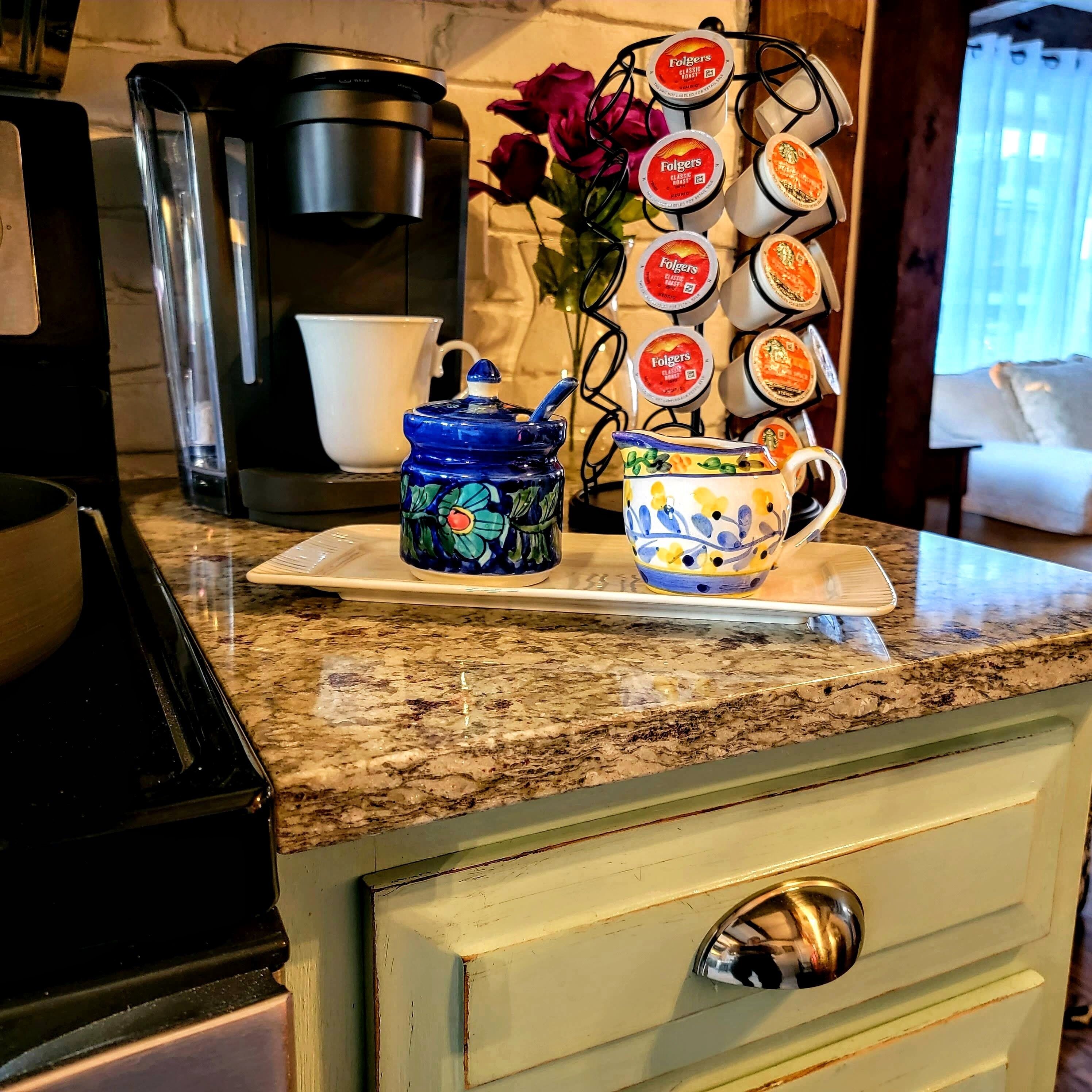 Una encimera de cocina con una cafetera, un hervidor de té y un escurreplatos con tazas de café Folgers.