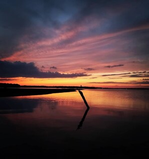 Un coucher de soleil sur une étendue d’eau calme, avec la silhouette d’un pont.