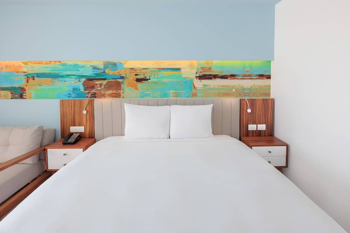 Habitación de hotel con una cama grande, dos mesitas de noche y un cuadro abstracto de colores en la pared.