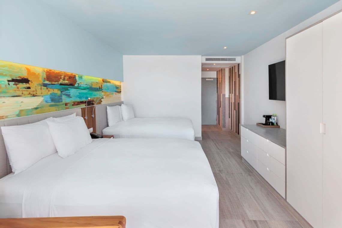 A modern hotel room with two beds, a large abstract painting on the wall, a flat-screen TV, and a wooden floor.