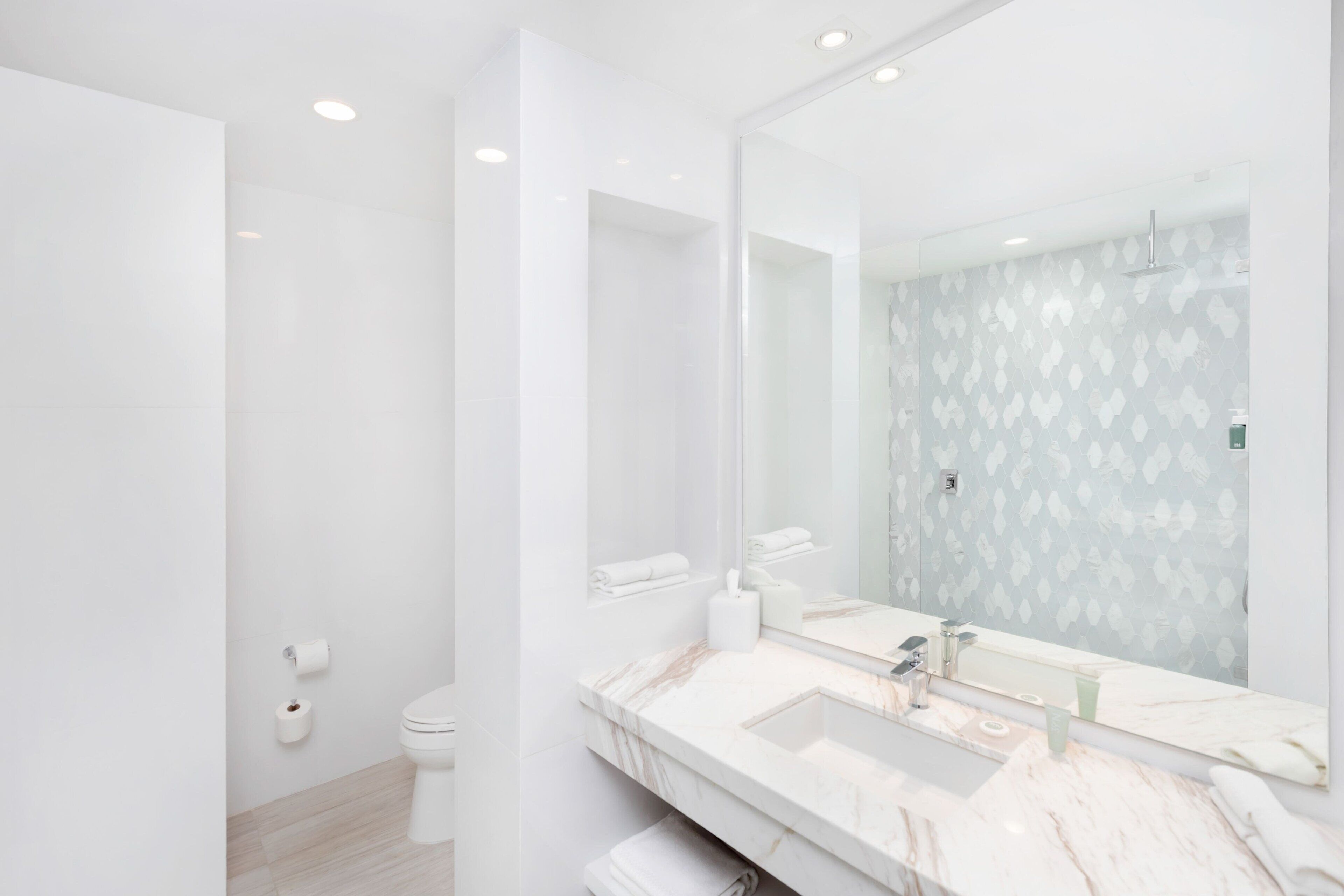 A modern bathroom with a large mirror, white fixtures, and a patterned wall.