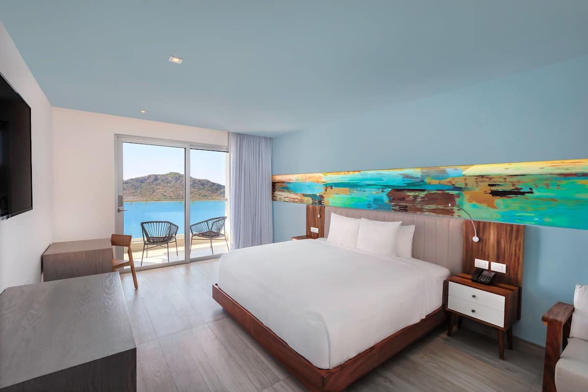 Habitación de hotel moderna con una cama grande, un escritorio y vistas al mar.