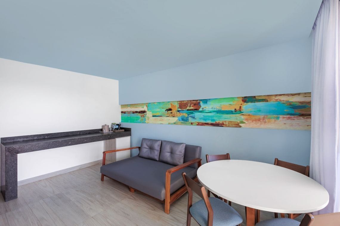 Una sala de estar moderna con un sofá, una mesa de comedor y un cuadro abstracto y colorido en la pared.