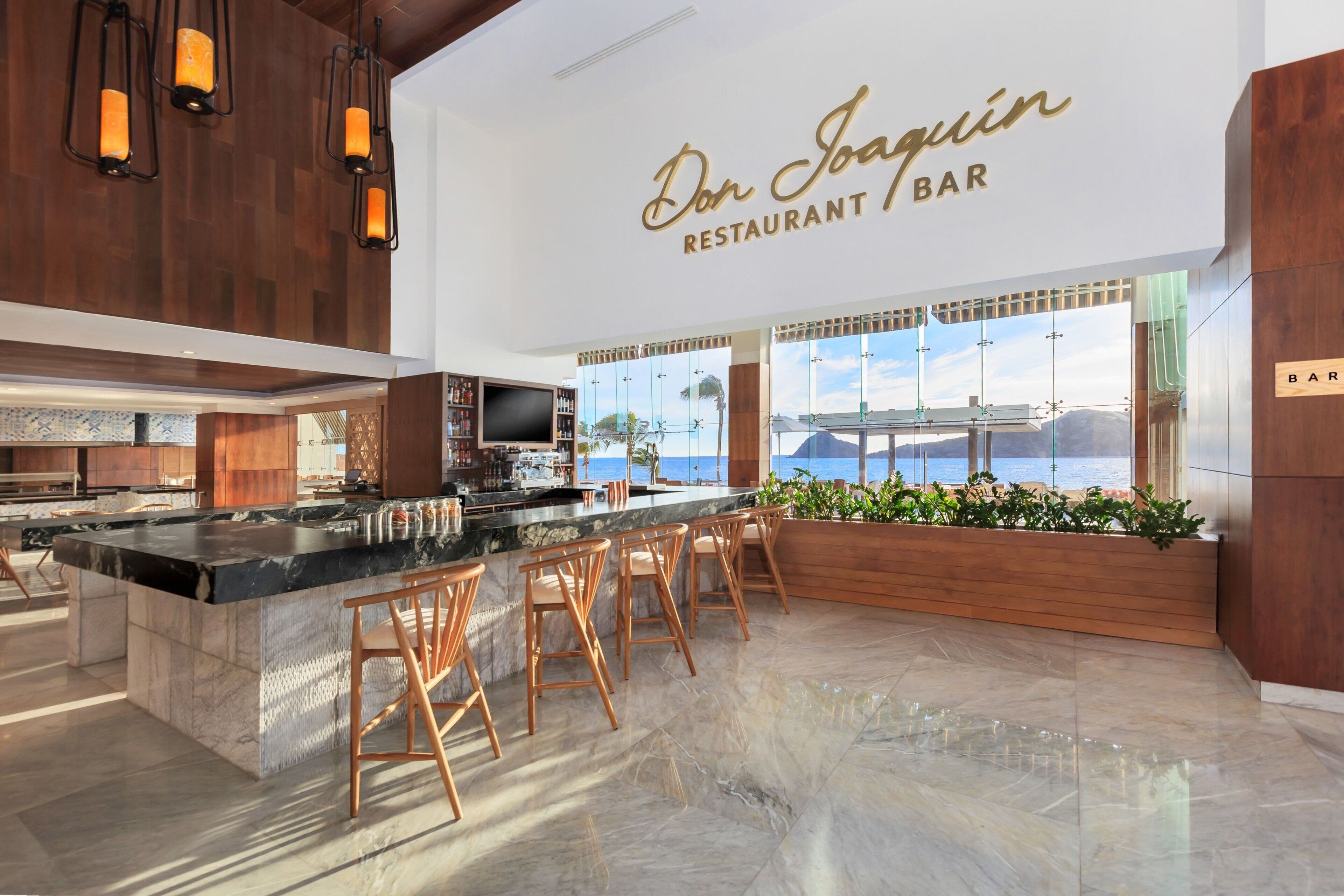 Ein modernes Bar- und Restaurant-Interieur mit einer großzügigen Barinsel, Holzelementen und Blick auf den Ozean.