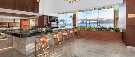 A modern bar and restaurant interior with a large island bar, wooden accents, and a view of the ocean.
