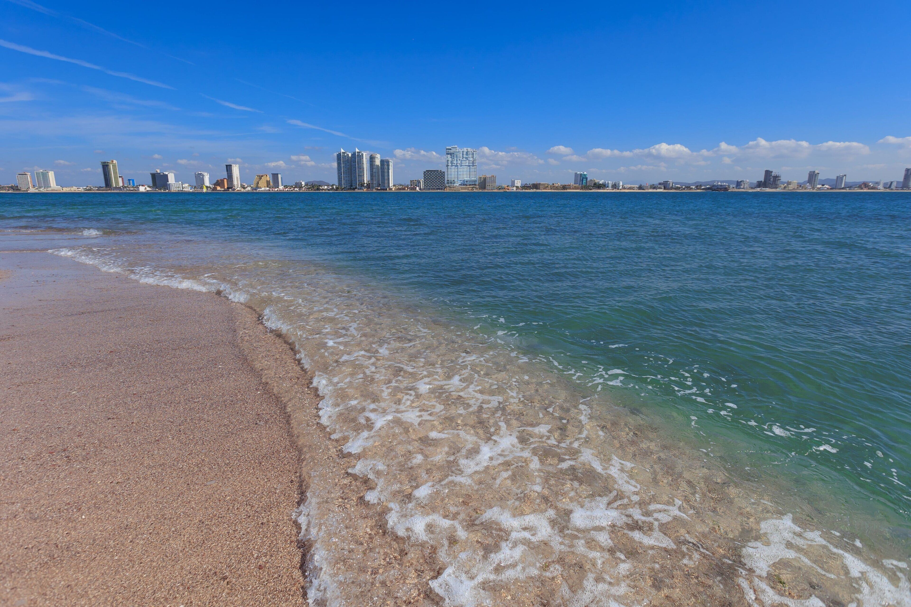 A beach with clear water and a city skyline in the background.