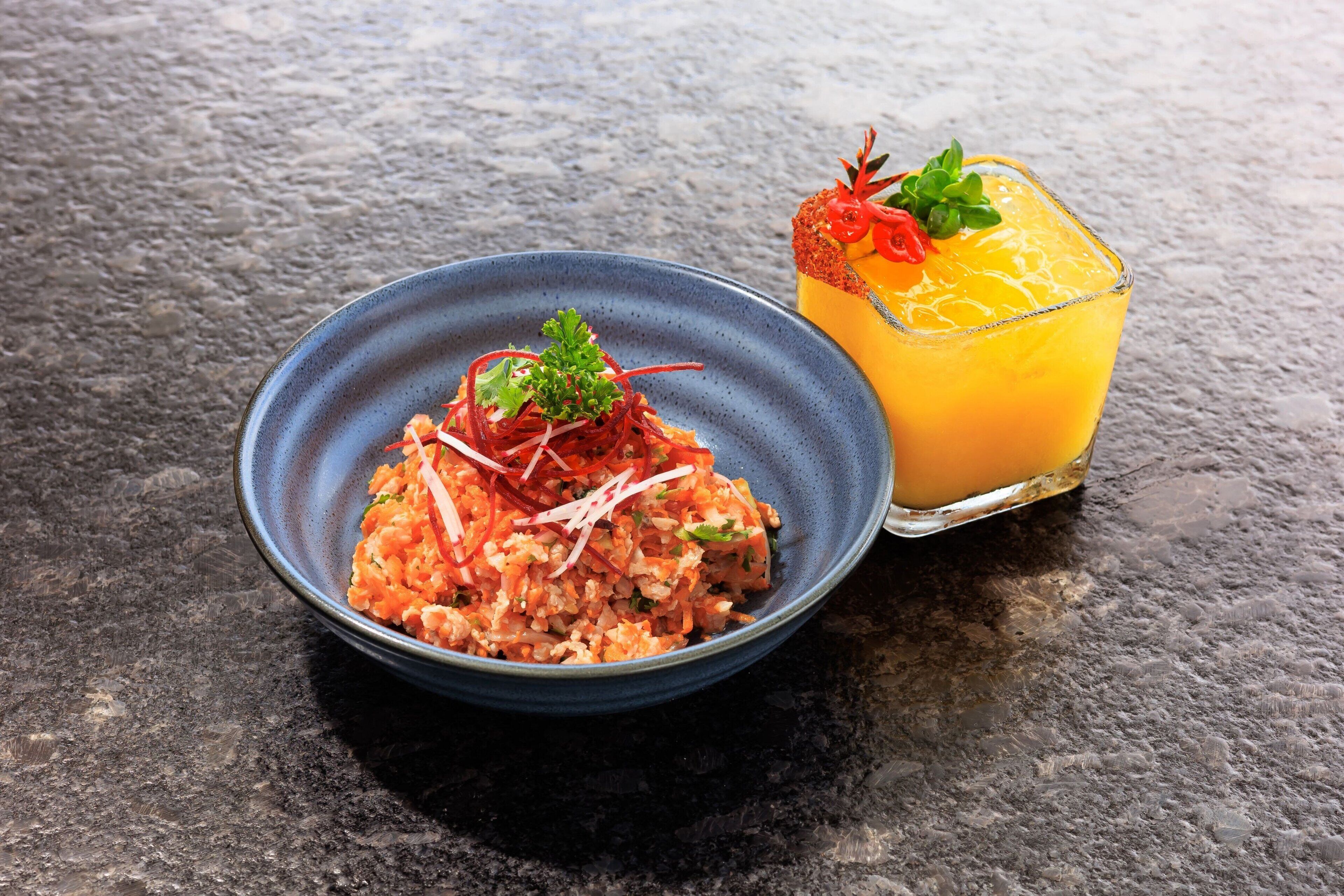Un plato de comida con decoración y un vaso de jugo de naranja sobre una superficie con textura.