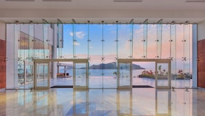A spacious lobby with a large glass door leading to an outdoor terrace with a view of mountains and a body of water.