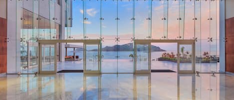 Un vestíbulo amplio con un gran ventanal que da a una terraza exterior con vistas a montañas y una masa de agua.