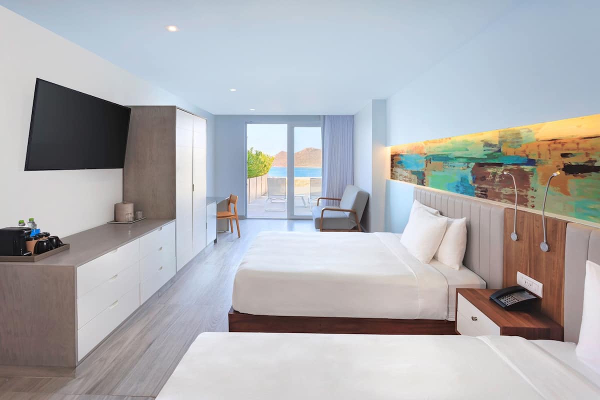 Habitación de hotel moderna con dos camas, un televisor de pantalla plana, un escritorio con una silla y vista al mar.