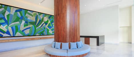 A modern lobby with a wooden cylindrical column, a seating area with blue cushions, and a colorful abstract mural on the wall.