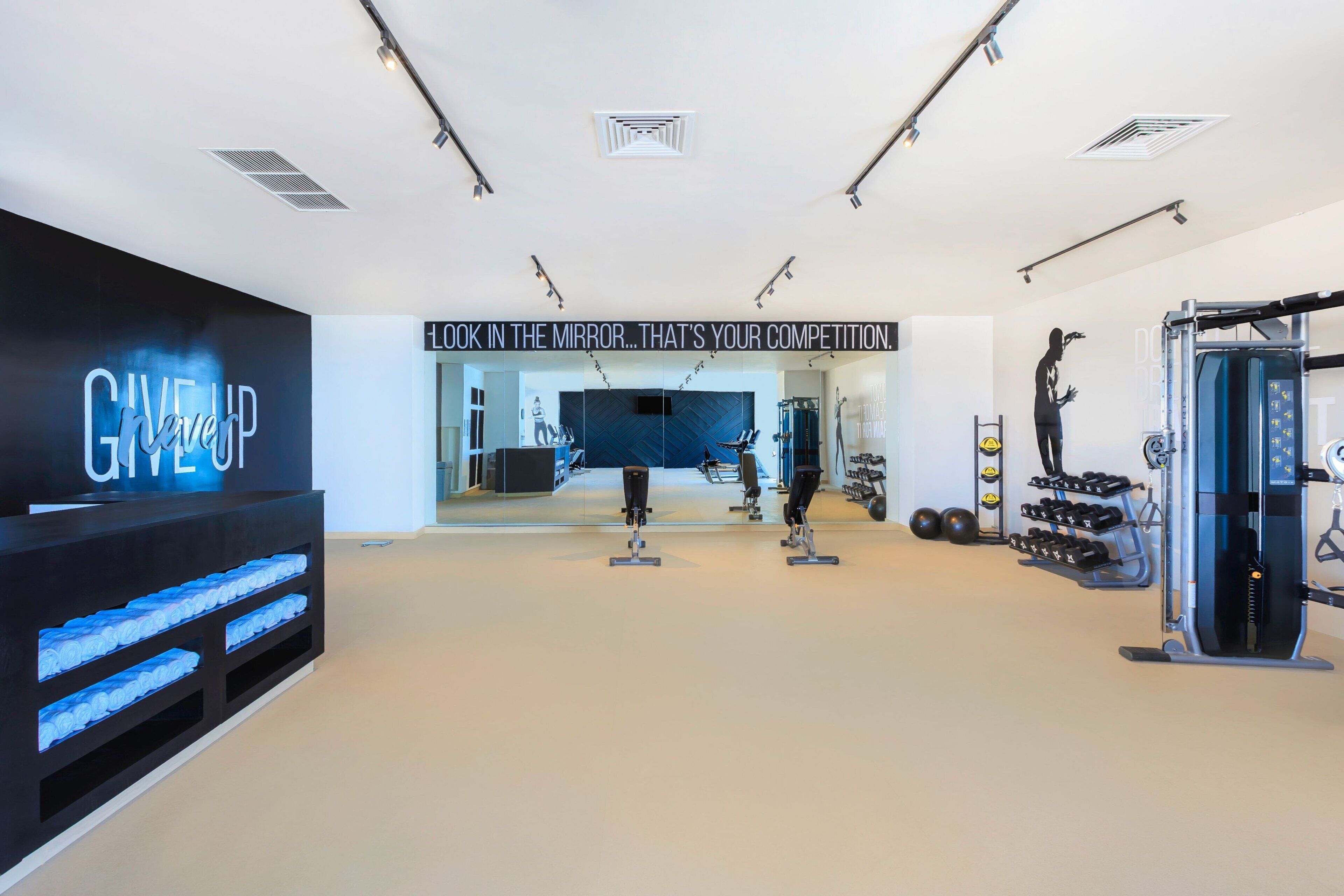 Academia moderna com equipamentos de exercício, um letreiro motivacional e uma parede com a inscrição 'GIVE UP'.