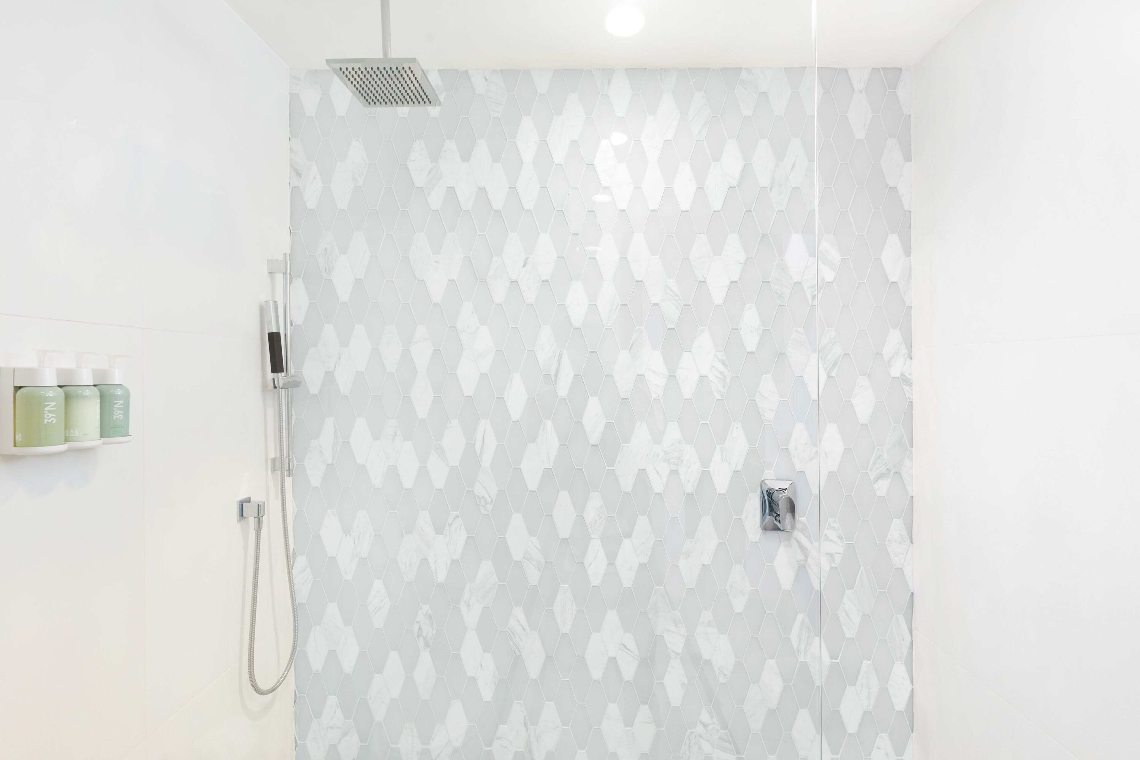 Ducha con patrón geométrico de azulejos, cabezal de ducha manual y panel de control en la pared.