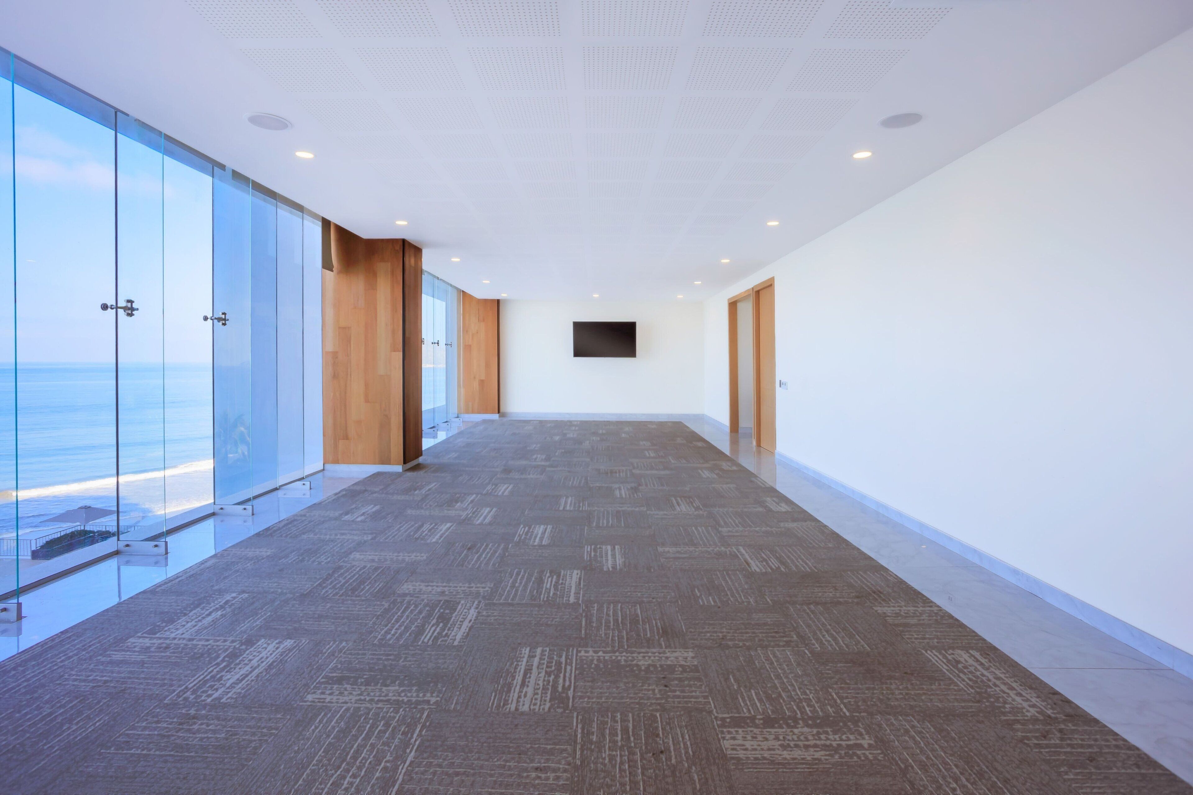 A modern hallway with glass walls, a patterned carpet, and wooden accents.