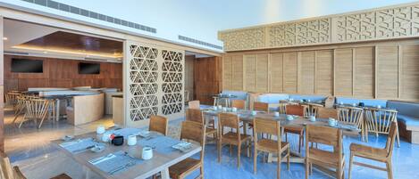 A spacious dining area with multiple tables and chairs, a kitchen area, and a decorative wall with geometric patterns.