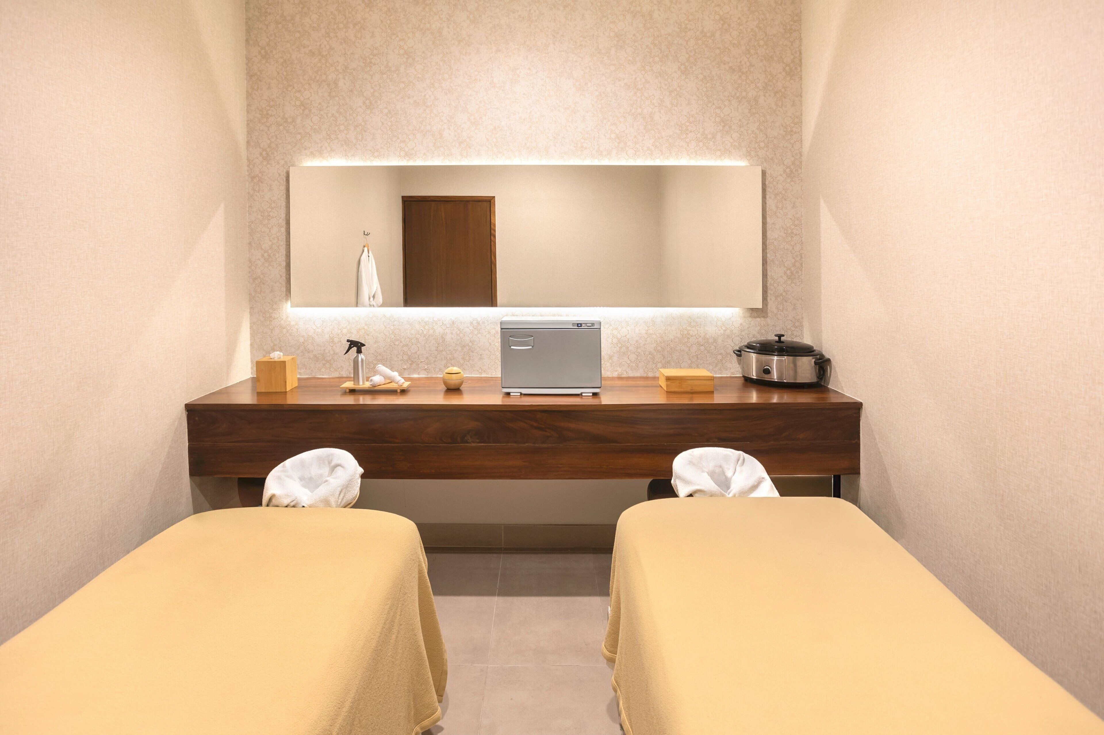 A hotel room with a wooden vanity, a laptop, a kettle, and two beds with towels.