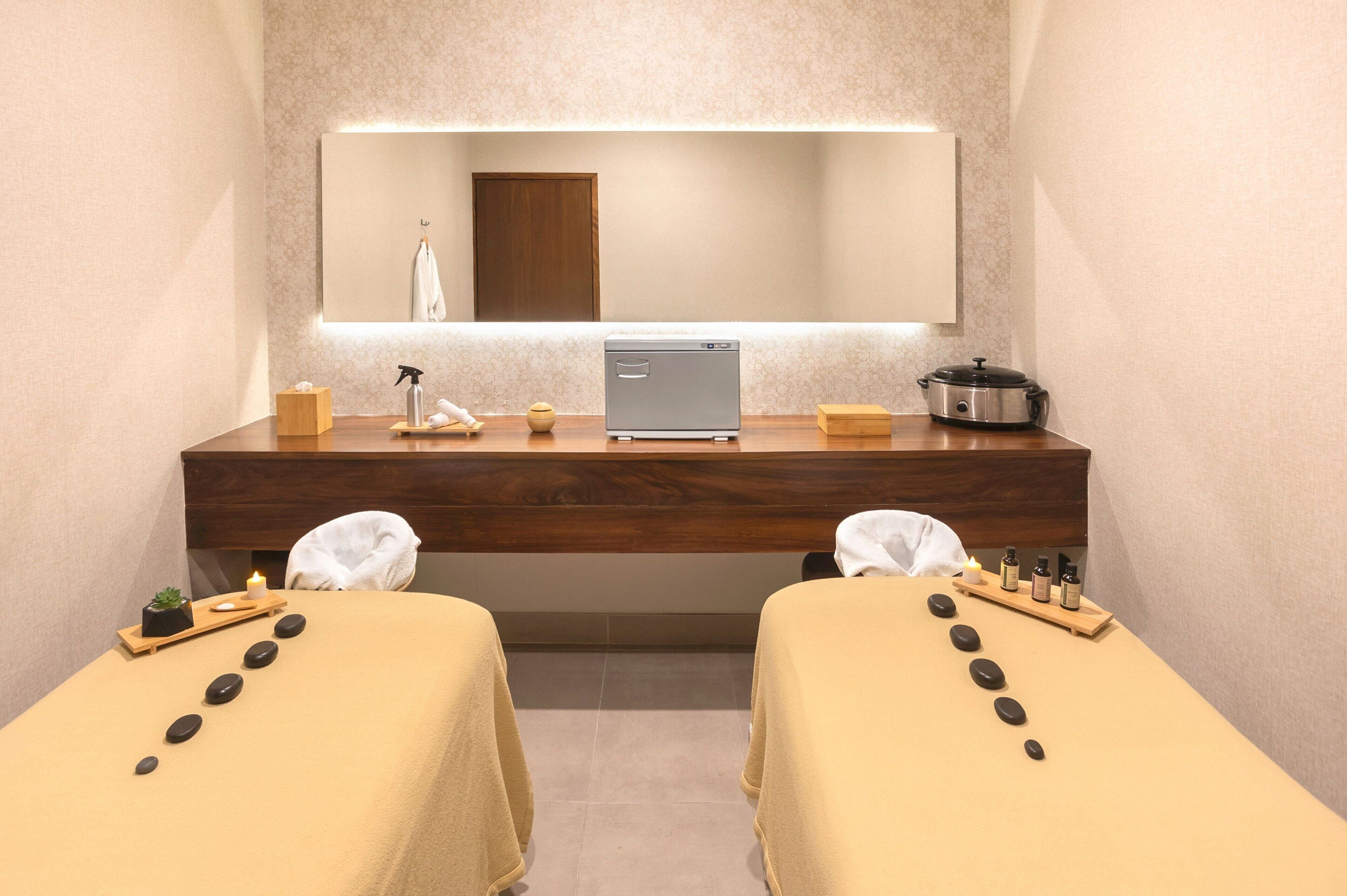 A spa room with two massage tables, a wooden counter, a small plant, a candle, and a massage machine.