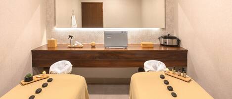 A spa room with two massage tables, a wooden counter, a small plant, a candle, and a massage machine.