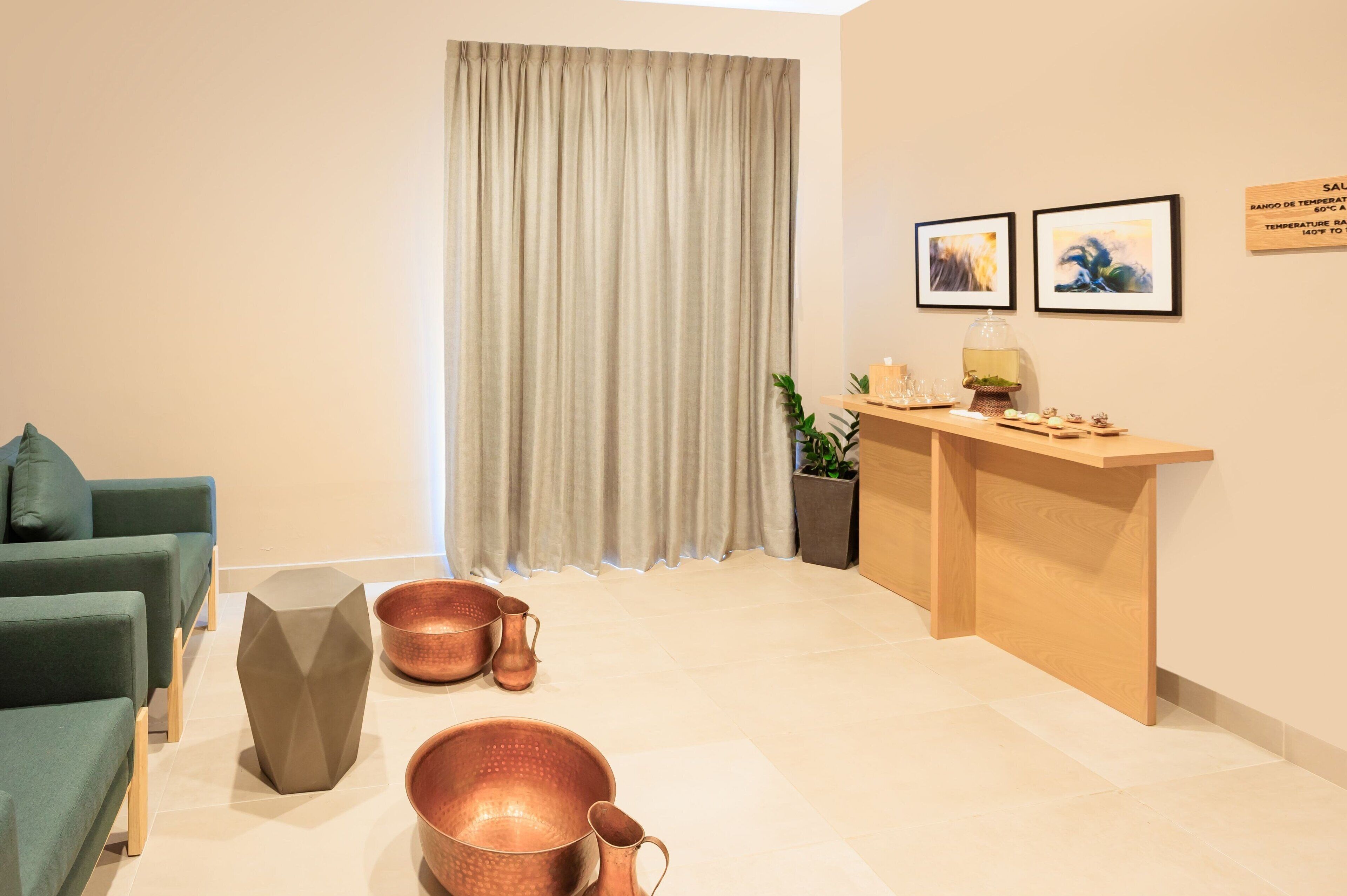 Uma sala de estar moderna com um sofá verde, um balcão de recepção de madeira e utensílios de cobre no chão.