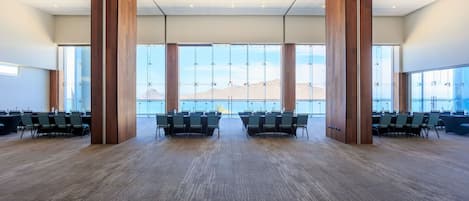 A spacious conference room with large windows, wooden pillars, and rows of chairs.