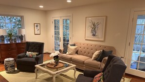 Ein Wohnzimmer mit einem dunklen Sessel, einem beige gefärbten Sofa und einem Glastisch mit Dekorationen.