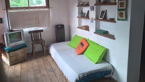 A bedroom with a bed, a desk, a chair, a television, and shelves with various items. - Casa Luciérnaga, ideal to enjoy the north of Argentina (humahuaca)