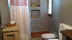 A bathroom with two toilets, a wooden cabinet, a shower curtain, and a small shelf with toiletries. - Casa Luciérnaga, ideal to enjoy the north of Argentina (humahuaca)