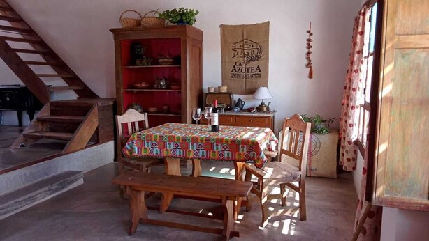 A dining area with a wooden table and benches, a red cabinet with shelves, a wall-mounted sign, and a staircase. - Casa Luciérnaga, ideal to enjoy the north of Argentina (humahuaca)