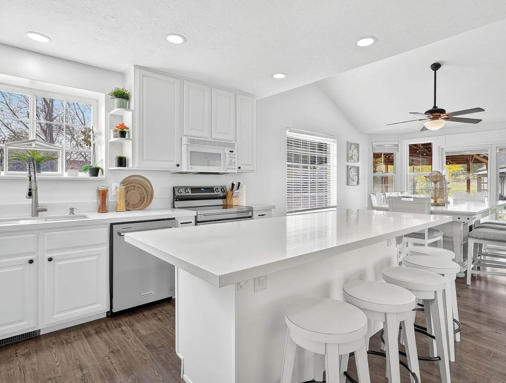 A modern kitchen with white cabinetry, a central island with bar stools, a built-in microwave, and a ceiling fan.