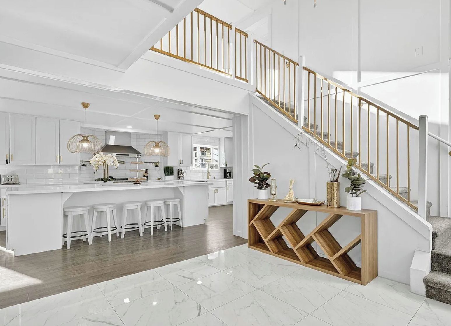 A spacious kitchen with a central island, white cabinetry, and a wooden staircase with a golden railing.