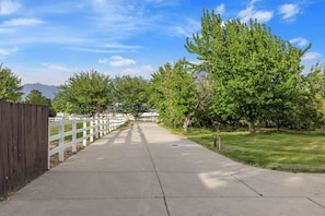 A paved pathway flanked by a white fence and trees, leading towards distant mountains.