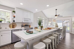 A modern kitchen with white cabinetry, a central island with stools, a built-in oven, and a ceiling fan.